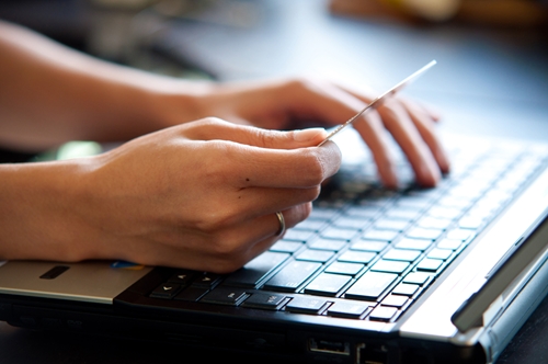 user typing on a laptop with one hand and holding a credit card in the other hand