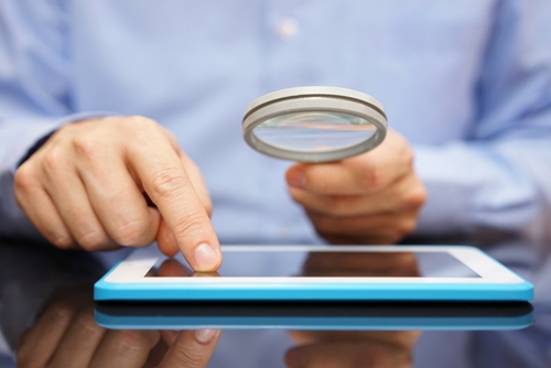 business person looking at a tablet with magnifying glass