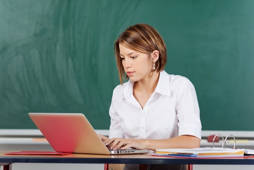 teacher sat at desk using a laptop