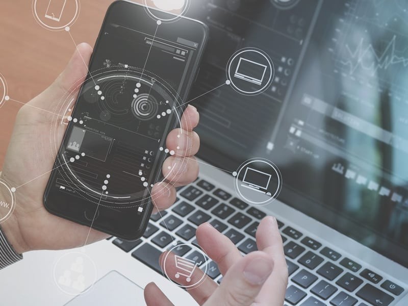 user holding a mobile phone next to a laptop keyboard see from above