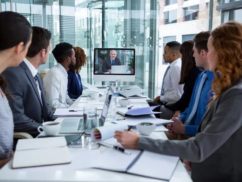 people on a video call looking at a screen at the end of the room